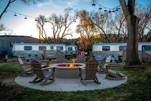 A fire pit surrounded by Adirondack chairs, with RVs parked in the background.