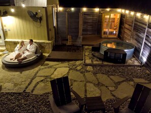 En udendørs patio med stengulv, jacuzzi, liggestole og en træterrasse.