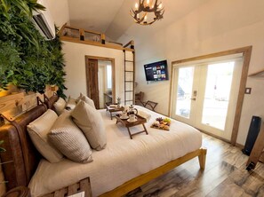 Un dormitorio con una cama grande, un televisor en la pared, un balcón y una escalera de madera.