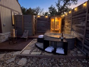 A hot tub with towels and wine bottles, surrounded by wooden walls and a stone deck.