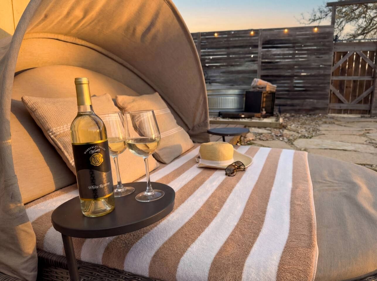 Una carpa con una botella de vino blanco y dos copas sobre una toalla a rayas.