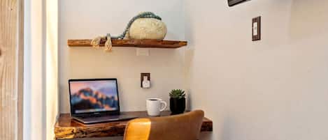 Un espacio de trabajo con una computadora portátil, una silla, una estantería con una planta y un televisor instalado en la pared.