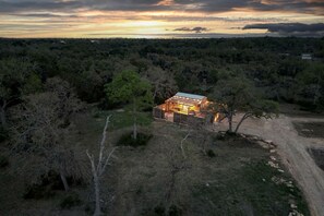 A remote cabin with a metal roof, surrounded by dense forest, accessible by a dirt path.