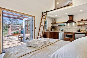 Une chambre avec un lit, une salle de bain, une cuisine et une porte-fenêtre coulissante donnant sur un espace extérieur.
