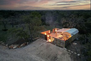 Una cabaña rústica con una amplia terraza, rodeada de árboles, al anochecer.