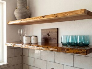 A kitchen with a wooden shelf, a wine glass, two condiment containers, and a sign with a deer logo.