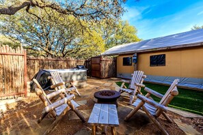 Une terrasse extérieure avec un foyer, des chaises en bois, un barbecue et un jacuzzi.