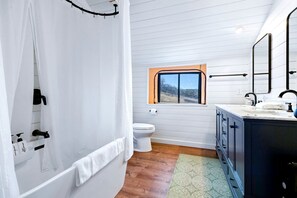 Une salle de bain avec douche, toilettes et lavabo, un plancher en bois et une fenêtre avec vue.