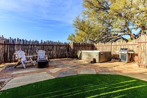 A backyard with a wooden fence, two Adirondack chairs, a fire pit, a grill, and a small shed.