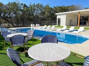 Un espace piscine aménagé avec des chaises longues et une table, entouré d’une clôture et d’arbres.
