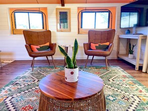A room with two leather chairs, a round wooden table, and a woven floor rug.