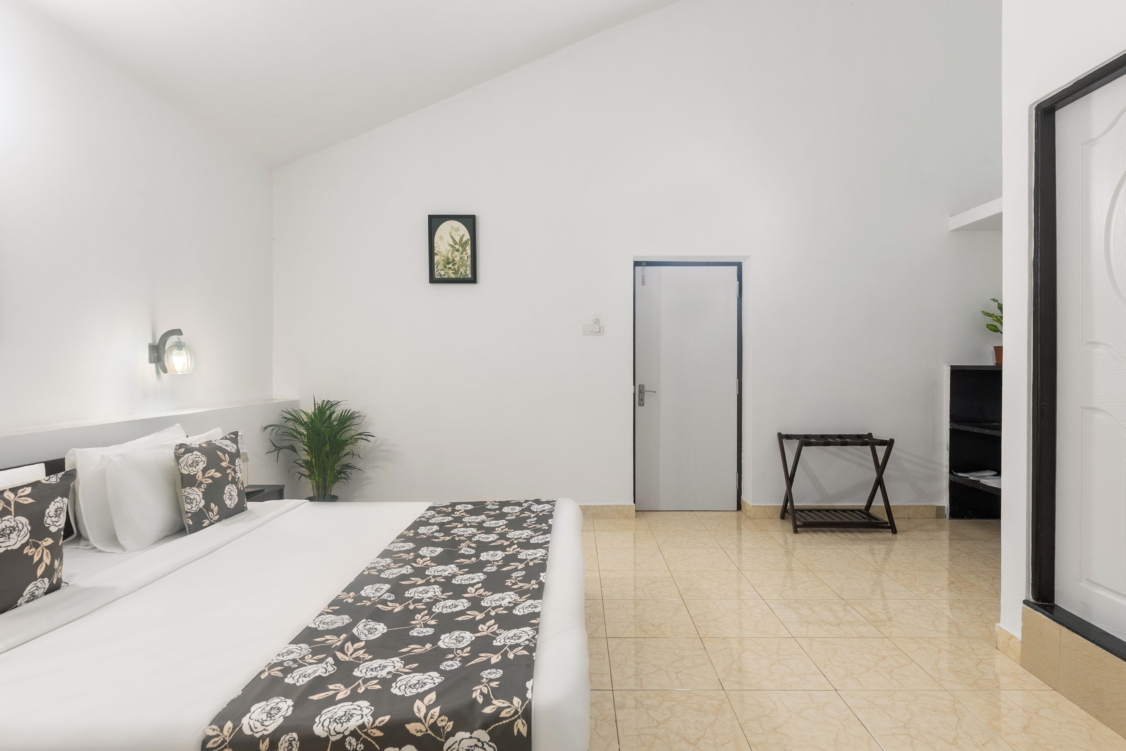 Ein Schlafzimmer mit Bett, Nachttisch, Lampe, einer Tür und einem kleinen Tisch mit Pflanze.