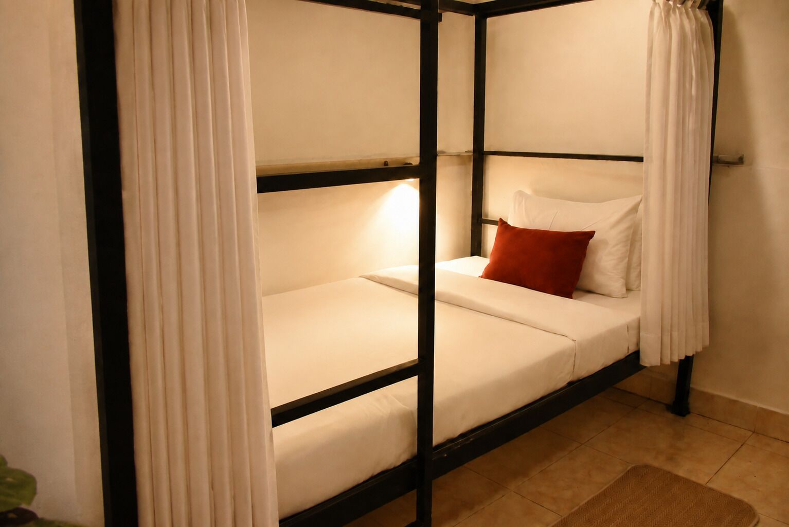 A single bed with a white mattress, black frame, and a red pillow.
