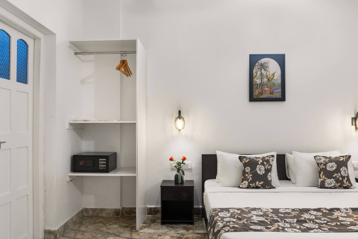 A hotel room with a bed, a nightstand, a shelf, a wall-mounted picture, and a door with a window.