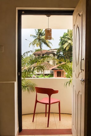 Puerta abierta que da a un balcón con una silla roja, una lámpara colgante y vistas a palmeras y edificios.