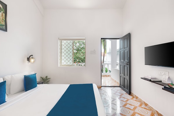 Habitación de hotel con cama, televisión, ventana y puerta que da a un balcón.