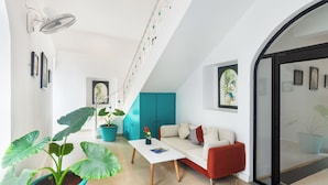 Un salon moderne avec un canapé blanc, un fauteuil rouge, une table basse blanche et une grande plante en pot.