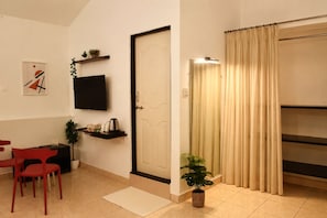 Habitación de hotel con televisión de pantalla plana, una puerta, ventana con cortinas, una mesita con planta y una silla roja.