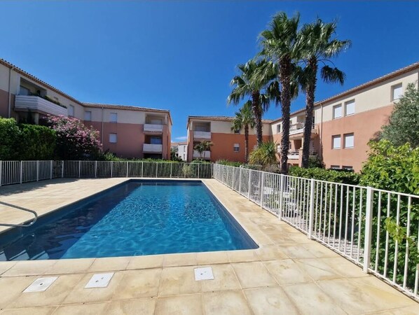 A rectangular swimming pool with a tiled deck, surrounded by a white metal fence.