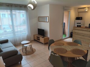 A modern living room with a sofa, TV, dining table, and chairs.