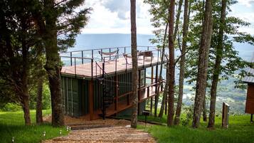 Una casa sull'albero con terrazza in legno e scale, immersa tra gli alberi e con vista sul paesaggio.