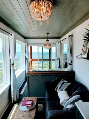 Una habitación acogedora con vista al mar, techo de madera, sofá negro y una cesta tejida.