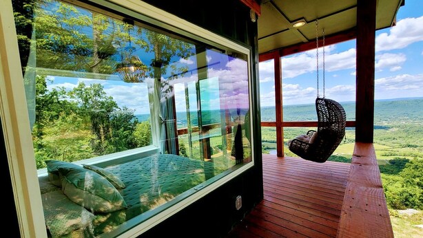 Ein Schlafzimmer mit großem Fenster, einem Hängekorbstuhl und Blick auf die Landschaft.