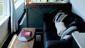Ein gemütliches Zimmer mit Meerblick, Holzbalkendecke, einer schwarzen Couch und einem gewebten Korb.
