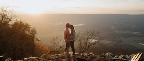 A couple standing by a campfire with a scenic view in the background.