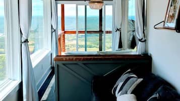 Una habitación acogedora con vista al mar, techo de madera, sofá negro y una cesta tejida.