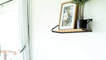 A modern living room with a grey sofa, a white throw blanket, a framed picture, and a potted plant on a wall-mounted shelf.