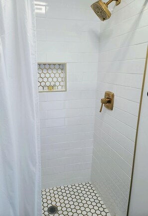 A shower with a gold showerhead, white tiled walls, and a hexagonal tile pattern on the floor. - Incredible Container with Rooftop and Beautiful Sunset Views in Georgia (Rising Fawn)