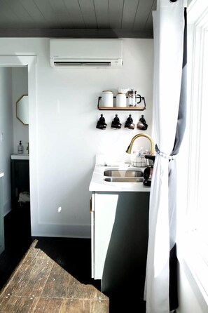 A small kitchen with a white countertop, a sink, and a white air conditioning unit mounted on the wall. - Incredible Container with Rooftop and Beautiful Sunset Views in Georgia (Rising Fawn)