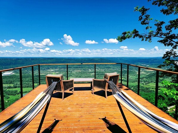 A wooden deck with two chairs and a bench, overlooking a green landscape.