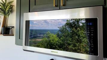 Una cucina moderna con un ampio forno a microonde in acciaio inossidabile, mobili verdi e vista sul paesaggio.