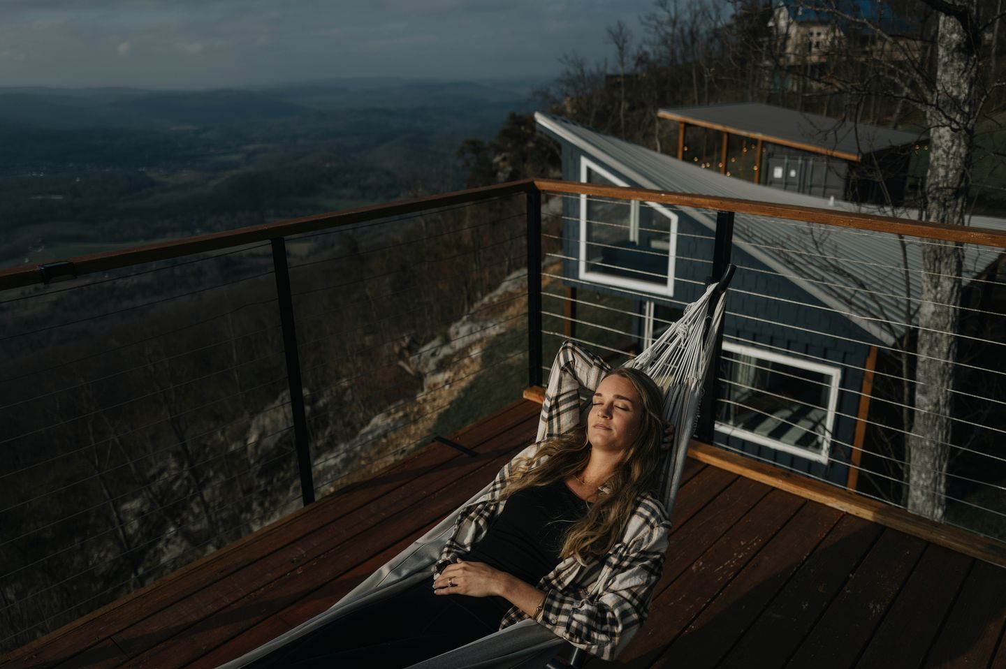 Eine Person entspannt in einer Hängematte auf einem Holzboden mit Blick auf eine gebirgige Landschaft.