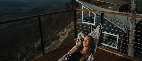 A person relaxing in a hammock on a wooden deck with a view of a mountainous landscape.