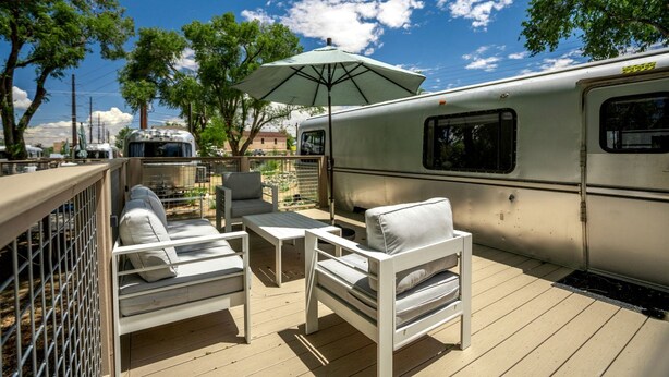 Eine Terrasse mit Gartenmöbeln, einem überdachten Bereich und einem Wohnwagen.