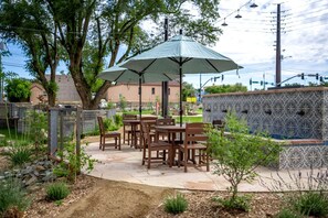 Une terrasse extérieure avec des tables et des chaises en bois, un grand parasol et un mur décoratif recouvert de carreaux.