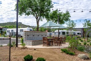 Un patio con mobiliario exterior, un muro de azulejos y vehículos recreativos al fondo.