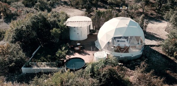 Una estructura de domo geodésico con una piscina circular y dos tanques de agua cilíndricos.