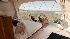 Une pièce aménagée sous une tente, avec un lit, une petite table, deux chaises et une vue sur le paysage.