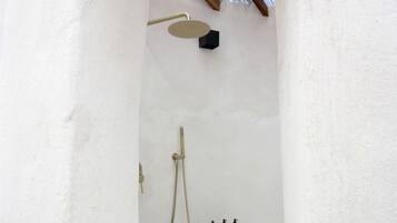 Une petite salle de bain aux murs blancs, équipée d’une douche, d’un porte-serviettes et de deux bouteilles de shampoing.