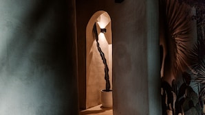 A hallway with a sculptural light fixture, an arched doorway, and a partial view of a wall with a textured pattern. - Exquisite Luxurious Dome with Outdoor Shower and Private Pool in Texas (Fischer)