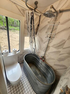 A compact bathroom with a shower, toilet, and a window with a view of trees.