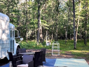Un área de camping con una caravana blanca, muebles de mimbre y una escalera metálica.