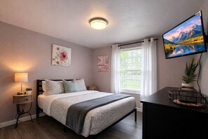 A bedroom with a bed, bedside tables, a TV, and a window with curtains.