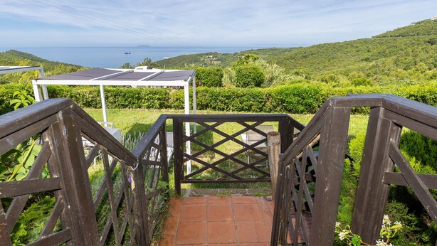 Un escalier en bois mène à une zone abritée d’où l’on peut admirer la mer et les collines.