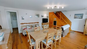 A room with a wooden dining table, chairs, a sofa, a TV, and a staircase. - Gîte 'Notre Désir' with Mountain View, Private Terrace and Wi-Fi (Abriès-Ristolas)