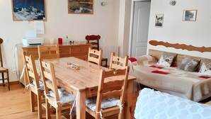 A room with a wooden dining table, chairs, a sofa, and a bed. - Gîte 'Notre Désir' with Mountain View, Private Terrace and Wi-Fi (Abriès-Ristolas)